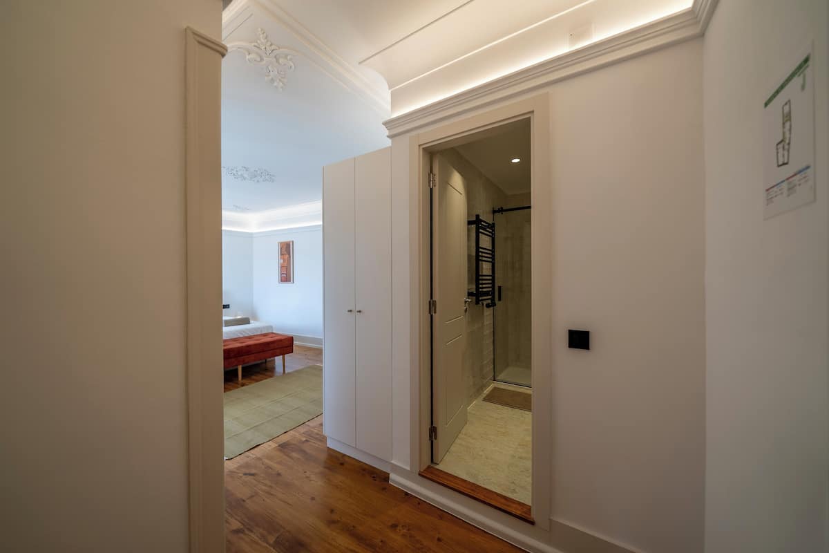 A hallway with a wooden floor leading to a room with a bed and a bench.