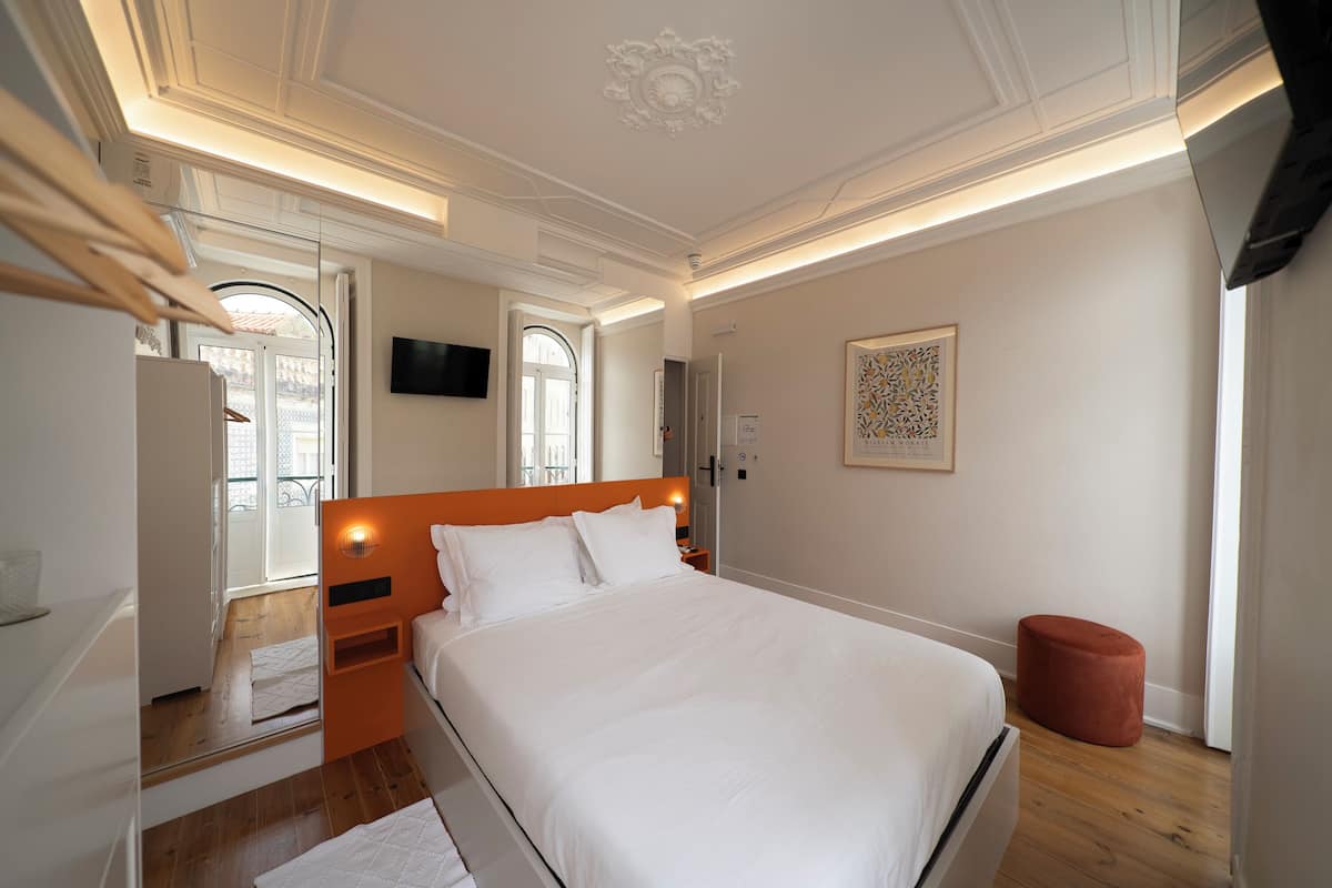 A modern bedroom with a large bed, a mirror, a television, and a red ottoman.