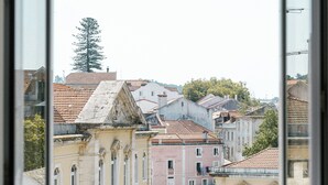 A view from a window overlooking a town with historic buildings and a prominent tree. - Good Old Days (Caldas da Rainha)