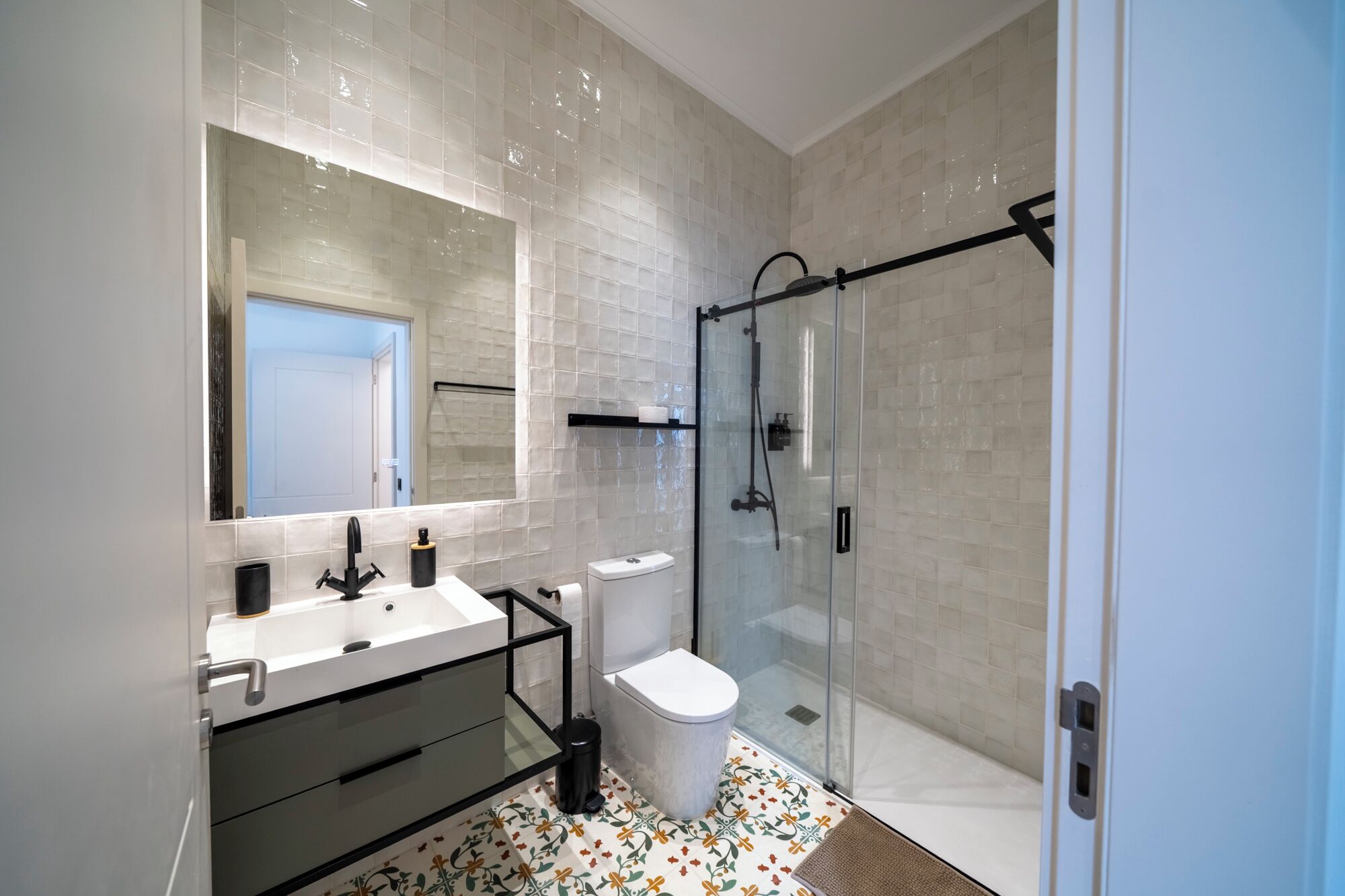 Een moderne badkamer met een douchecabine van glas, een wit wastafelmeubel en een zwarte kraan, en een toilet.