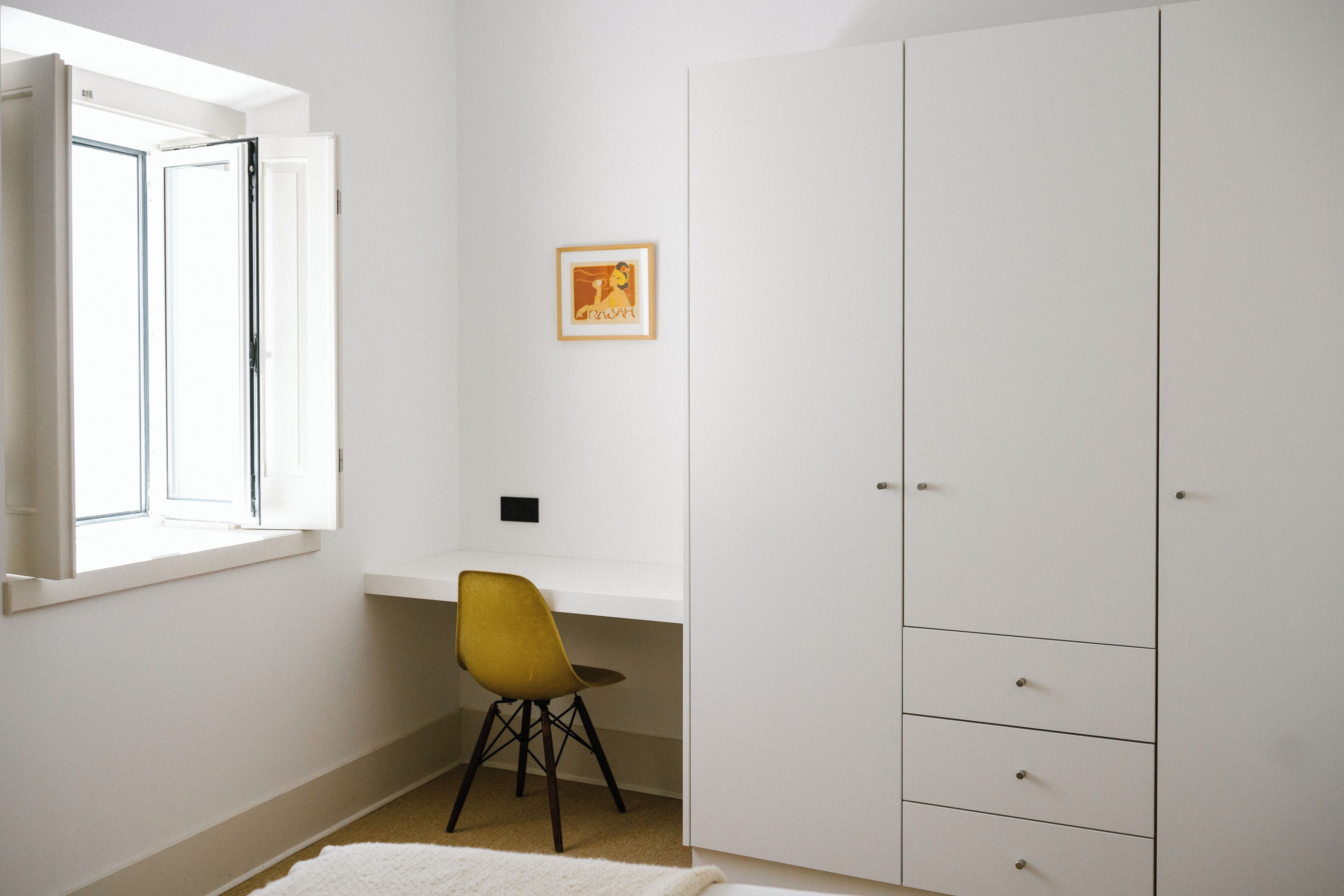 A room with a white wardrobe, a yellow chair, a small table, and a framed picture on the wall.