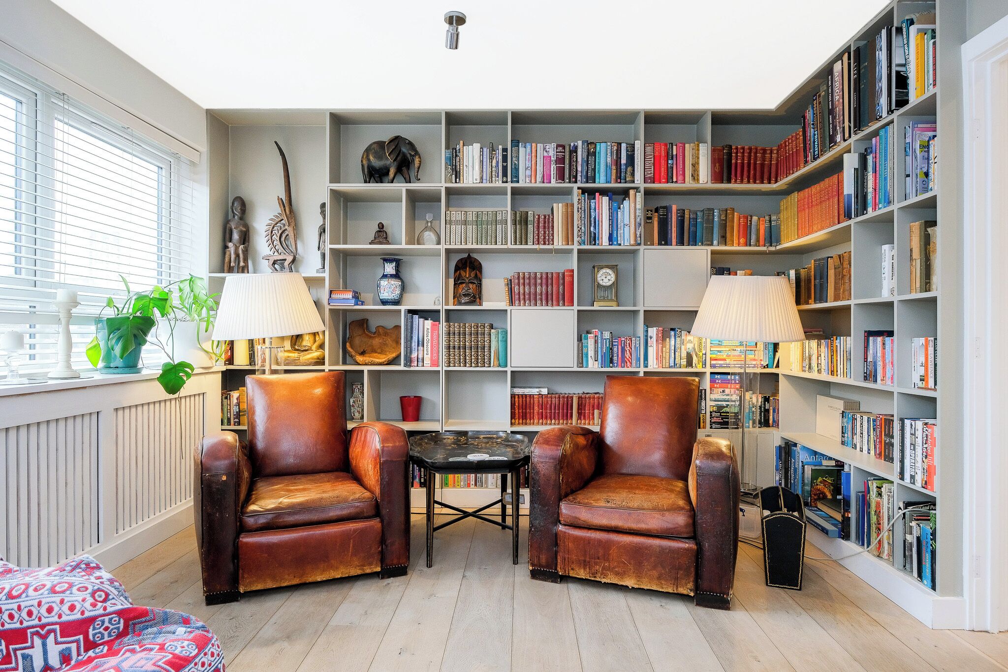 Un coin lecture confortable avec des fauteuils en cuir, une petite table et une bibliothèque remplie de livres.