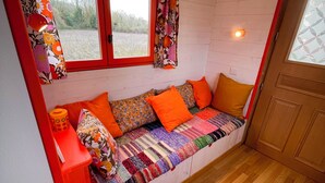 A cozy room with a wooden bench, a red stool, and a window with curtains.