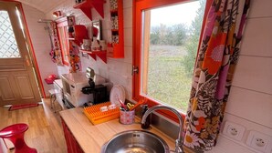 A compact kitchen with a sink, a window with a floral curtain, and a red countertop.