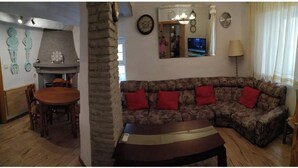 Un salon avec une cheminée en pierre, un canapé avec des coussins rouges, une table à manger avec des chaises et un téléviseur fixé au mur.
