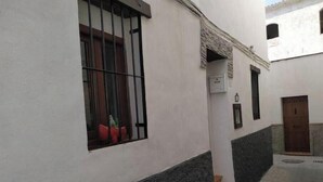 Une ruelle étroite avec un bâtiment blanc orné d’une fenêtre avec des barreaux en métal, d’une petite porte et d’un pot de fleurs.