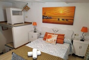 A bedroom with a bed, two bedside tables, a nightstand, a TV, and a painting of a sunset over water. - Casilla de Nigüelas  (AN)