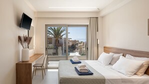 Habitació d'hotel amb llit, escriptori, cadira, televisió i un balcó amb vista a palmeres i edificis.