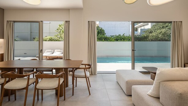 Habitació d'hotel moderna amb zona de menjador, sofà i vista a una piscina.