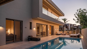 Una casa moderna amb piscina, mobiliari exterior i entrada amb porta de vidre.