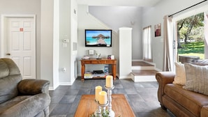A living room with a sofa, a coffee table with candles, a TV, and a wooden console table. - Family Getaway Less than 5 miles from Disney! (Kissimmee)