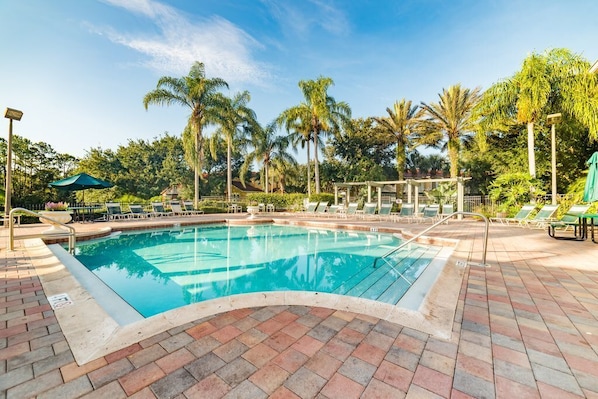 A swimming pool with lounge chairs and umbrellas, surrounded by palm trees.