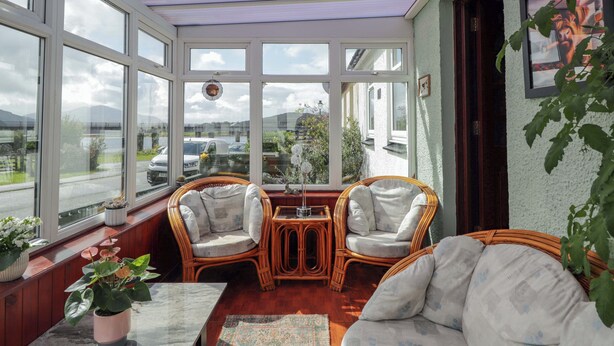 Un solárium con ventanas amplias, mobiliario de mimbre y vistas al exterior.