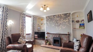 Una sala de estar con sofás de cuero, un televisor de pantalla plana, una chimenea y estantes decorativos.