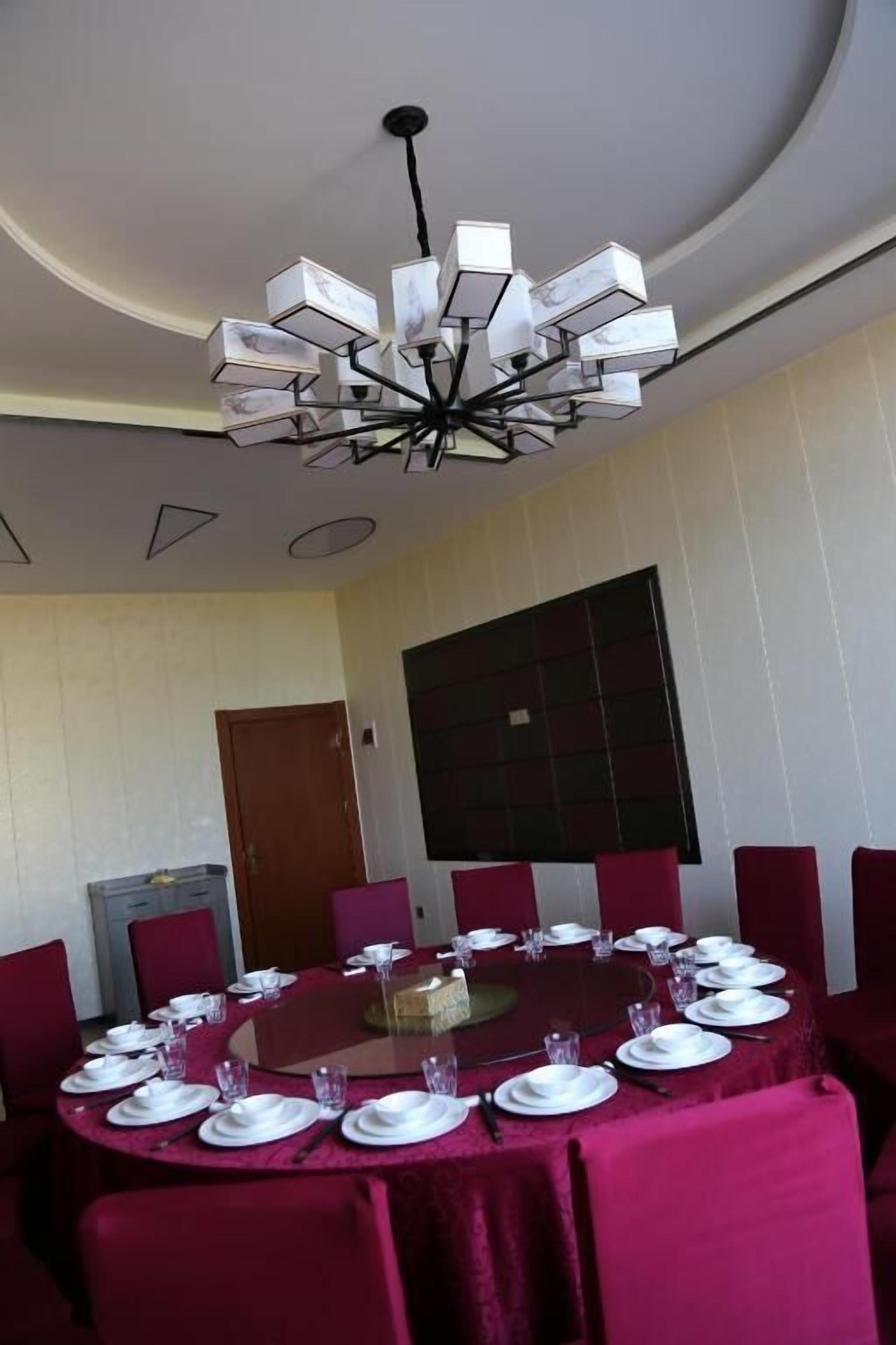 Un coin repas avec une table ronde dressée pour le repas, des chaises à revêtement rouge et un lustre moderne.
