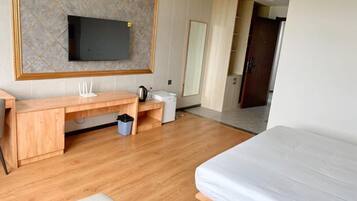 A hotel room with a wooden desk, a bed, a TV mounted on the wall, and a mirror.