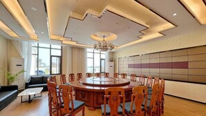 Μια αίθουσα συνεδριάσεων με ένα στρογγυλό τραπέζι, ξύλινα καθίσματα και ένα πολυέλαιο.