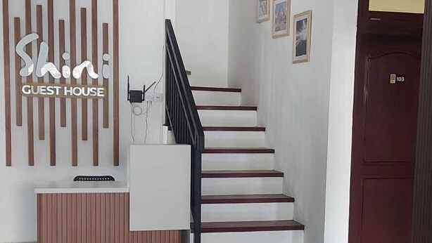 A modern hotel lobby with a reception desk, a staircase, and a door marked with the number 103. - Shini Guest House (Malang)