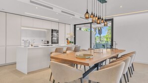 A modern kitchen with white cabinetry, a wooden dining table, and six chairs. - Villa Soul (Marbella)