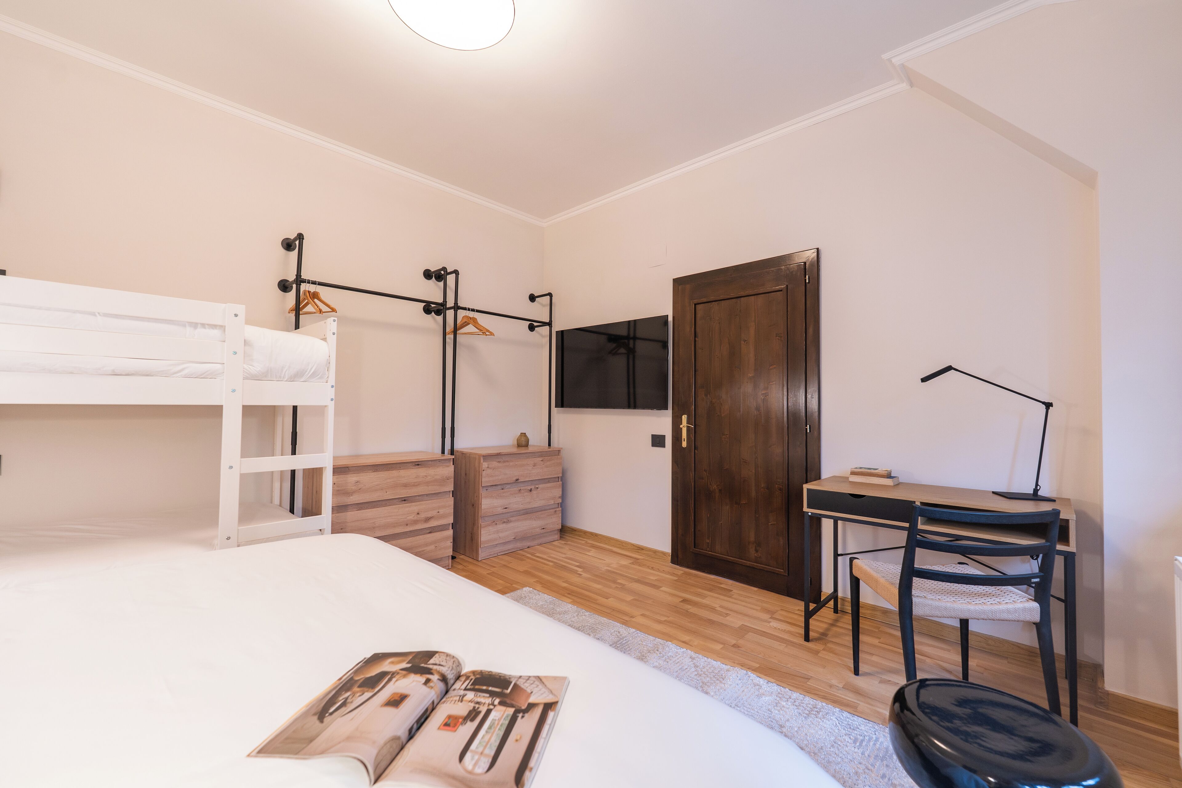A bedroom with a bunk bed, a wooden dresser, a desk with a chair, and a television on the wall.