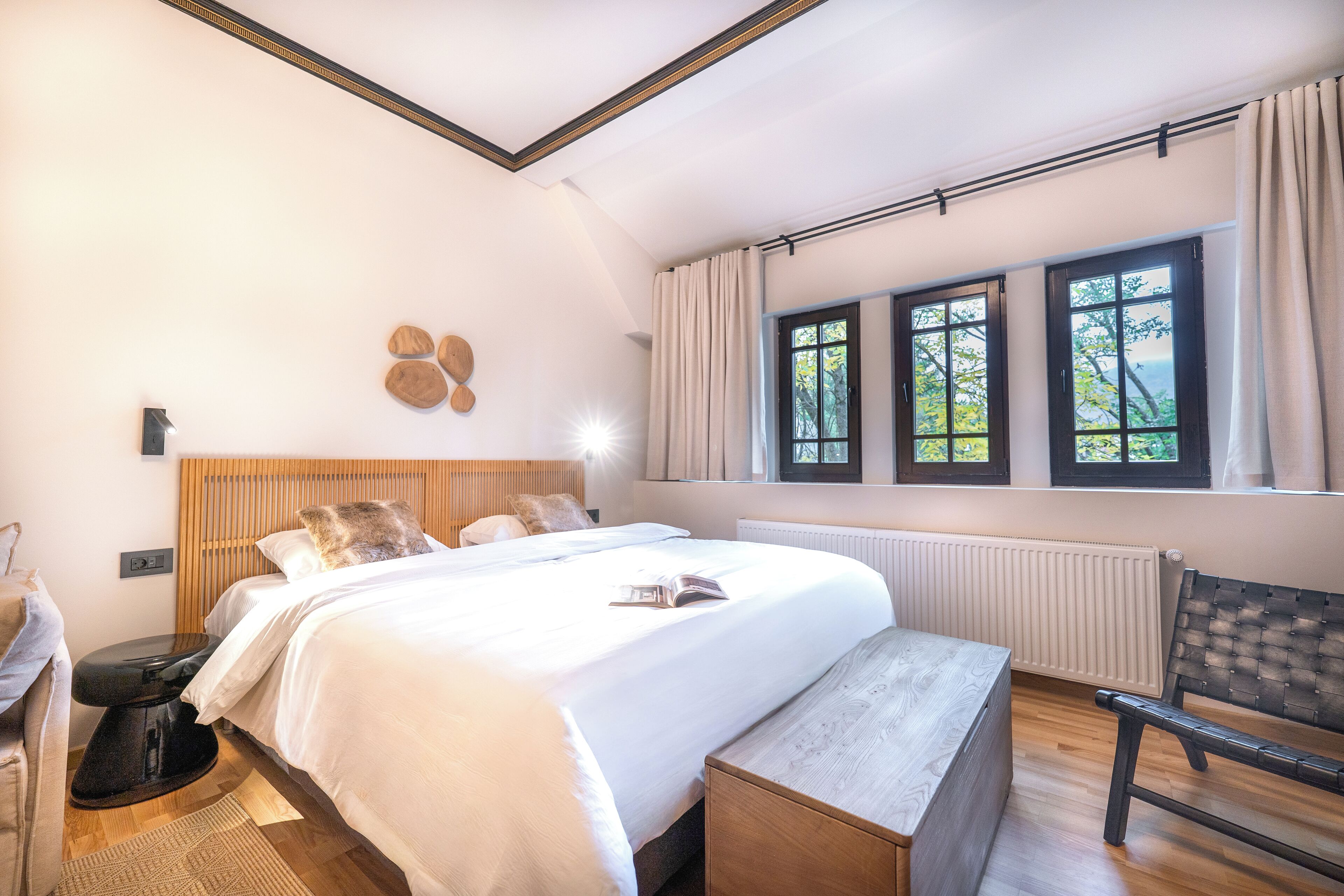 Un dormitorio con una cama grande, un banco, una silla y un ventanal con cortinas.