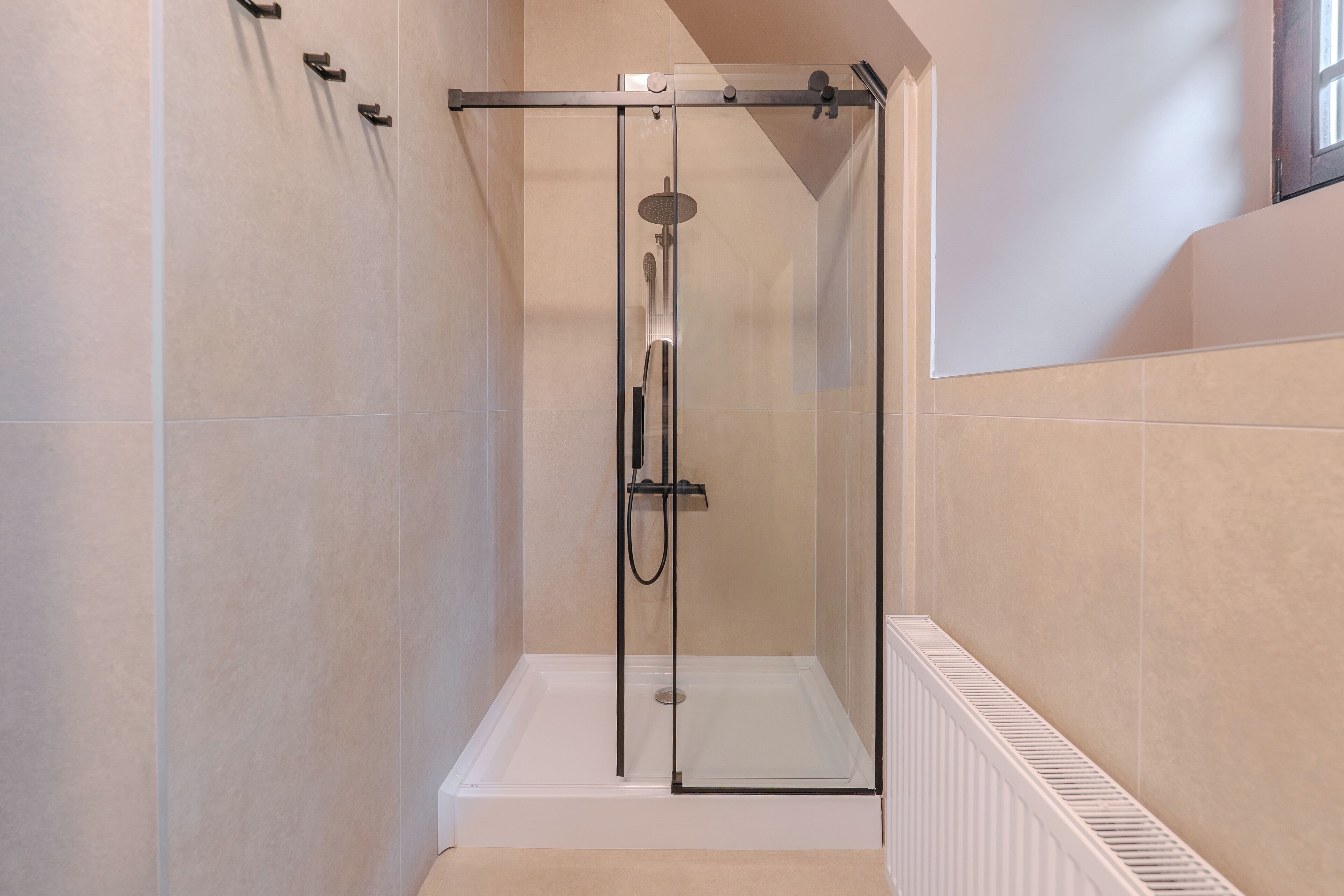 A glass-enclosed shower with a white base, beige walls, and a white radiator.