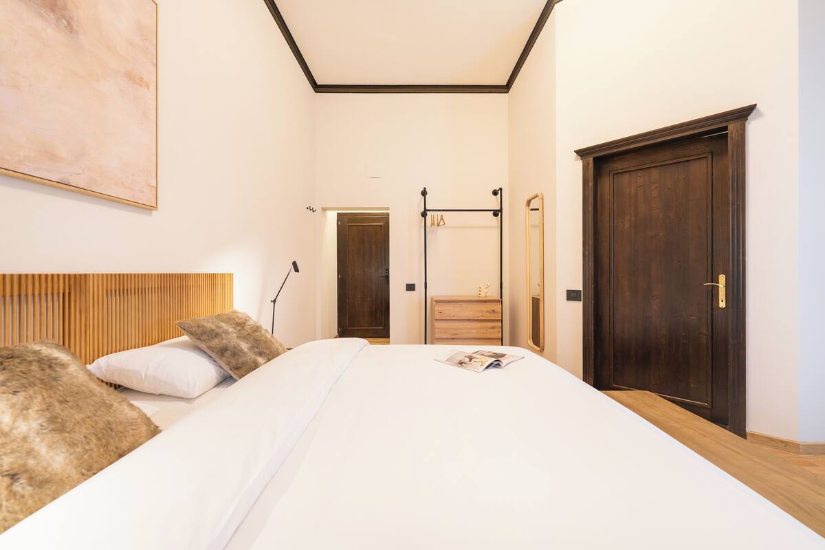 Une chambre avec un grand lit, une tête de lit en bois et une commode en bois. Il y a une porte et un miroir sur le mur.