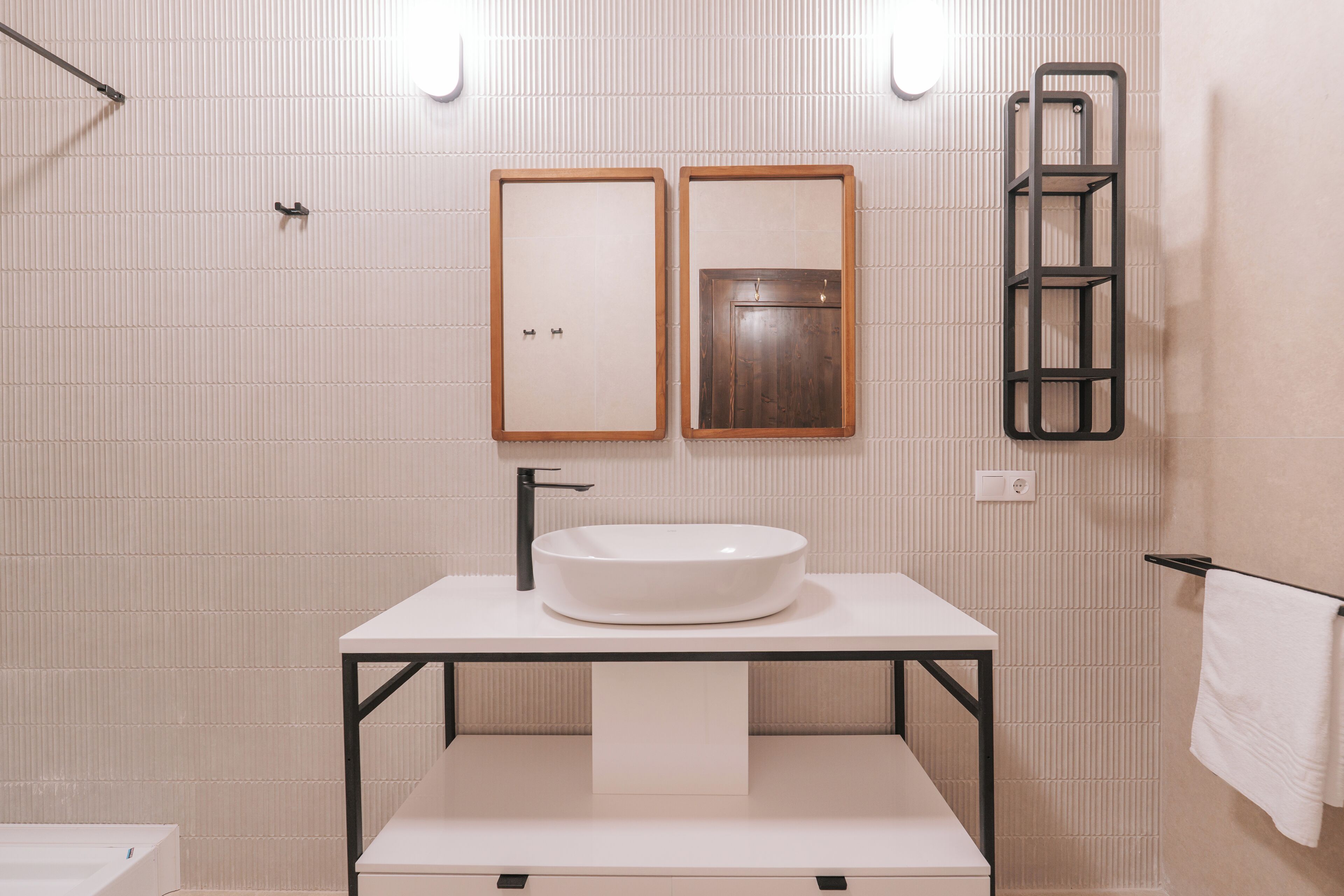 A modern bathroom with a white sink, two mirrors, a towel rack, and a towel hanging on it.