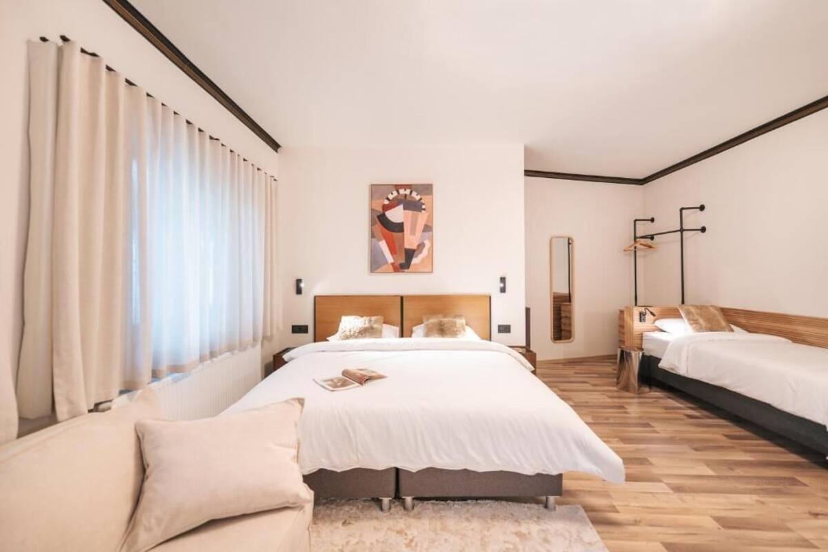 Une chambre d’hôtel moderne avec un grand lit, un lit plus petit, un canapé et une grande fenêtre avec des rideaux.