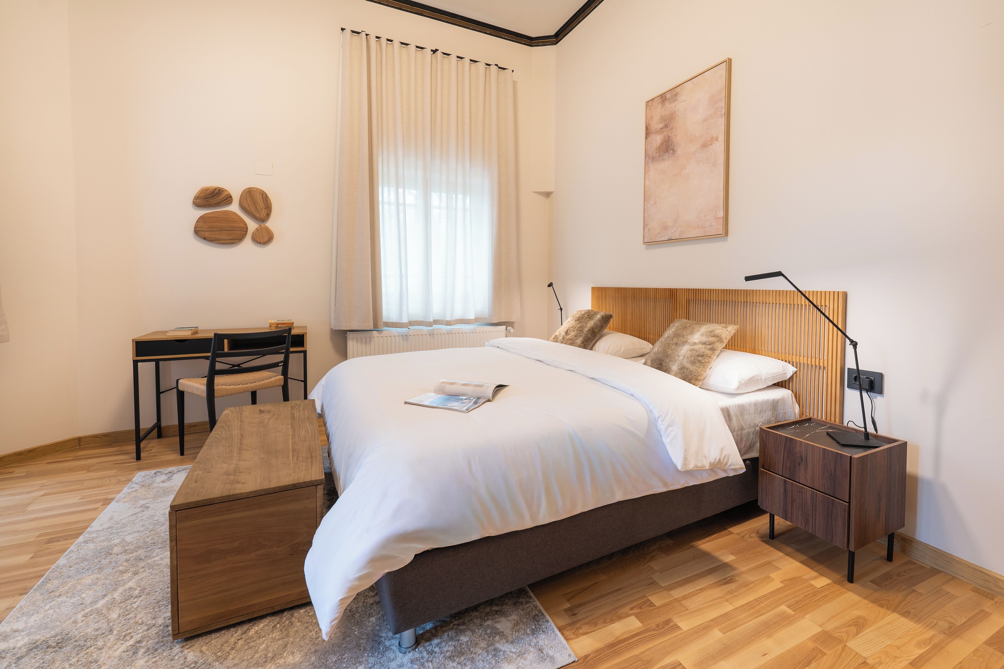 Un dormitorio moderno con una cama de madera, mesitas de noche, un escritorio y un ventanal con cortinas.