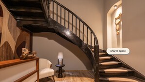 A curved wooden staircase with a black railing, a small round table with a lamp, and a chair in a room with wooden flooring and a beige wall. - Chateau Sinaia (Sinaia)