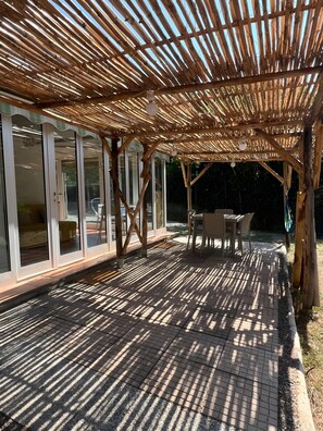 Een overdekt buitengebied met een houten pergola, glazen deuren en een betegeld terras.