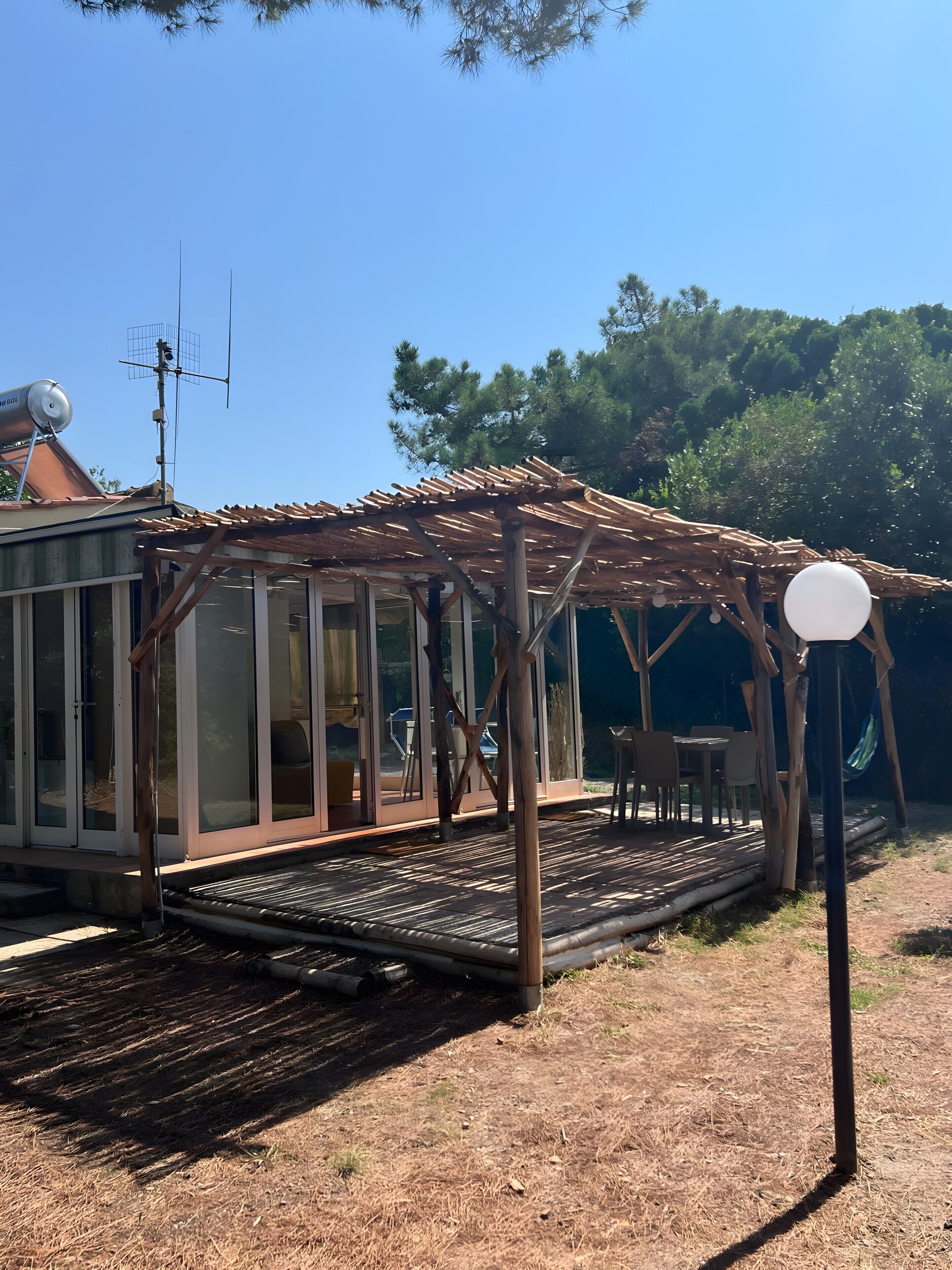 Et overdækket udendørs opholdsområde med pergola, en vandtank på taget og en hængekøje.
