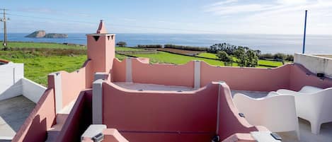 A rooftop terrace with a view of the sea, a small island, and a pink building.