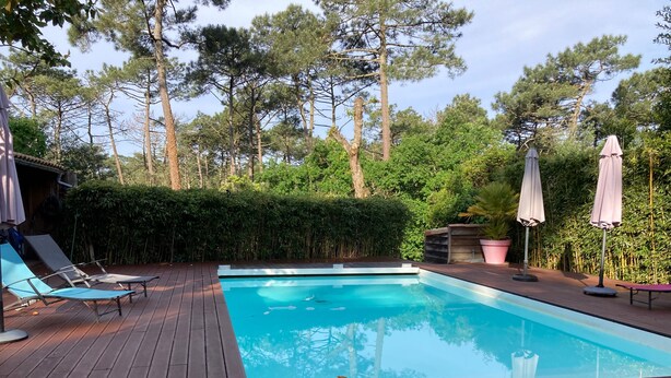A swimming pool with a wooden deck, lounge chairs, and umbrellas.