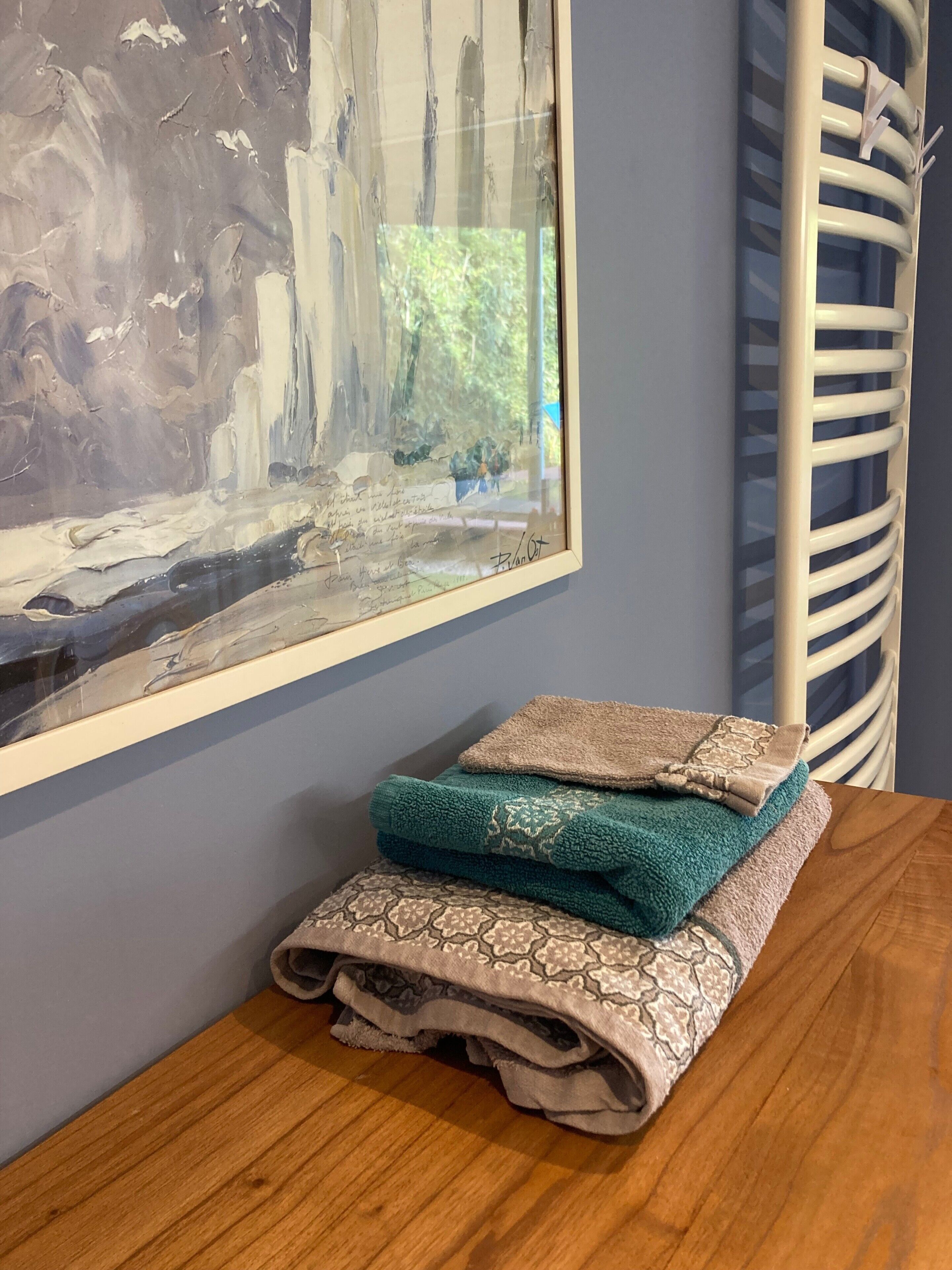 Un tableau abstrait encadré accroché au mur, une table en bois avec des serviettes pliées, et une chaise blanche.