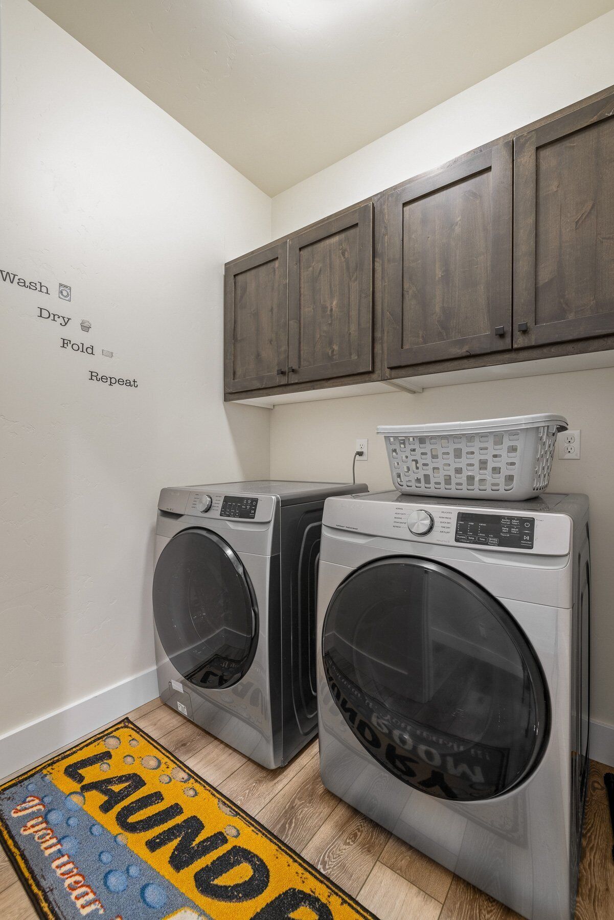 A laundry area with two front-loading washing machines, a drying rack, and a wall-mounted cabinet.