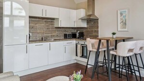 Eine moderne Küche mit weißen Schränken, einer Holzrückwand, einer eingebauten Mikrowelle und einer Bar mit Hockern.