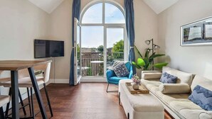 Ein Wohnzimmer mit Fernseher, Esstisch, einer Couch und einem großen Fenster mit Vorhängen.