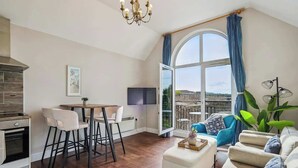 Eine moderne Küche mit Essbereich, ein großes Fenster mit Vorhängen, eine Couch und ein Fernseher.