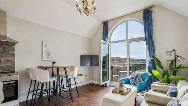 Eine moderne Küche mit Essbereich, ein großes Fenster mit Vorhängen, eine Couch und ein Fernseher.