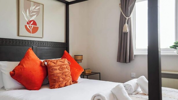 Ein Hotelzimmer mit Bett, Kissen, einem gerahmten Kunstwerk, einem Nachttisch und einem Fenster mit Vorhängen.