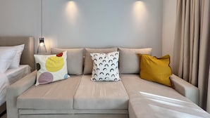 A modern hotel room with a beige sofa, two wall-mounted lights, and a bed with white bedding.