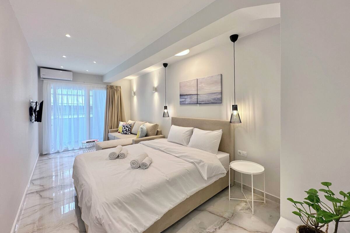 A modern bedroom with a large bed, a sofa, a small table, and a potted plant.