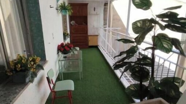 Un petit balcon avec du gazon synthétique, une chaise, une plante en pot et un meuble en bois.