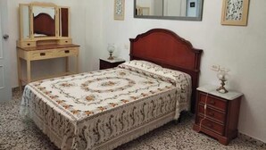 Une chambre à coucher comprenant un lit, une commode, une table de chevet, un miroir et un lustre.