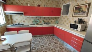 Une cuisine de taille réduite avec des meubles rouges, un plan de travail blanc, un four à micro-ondes et un sol à motifs.