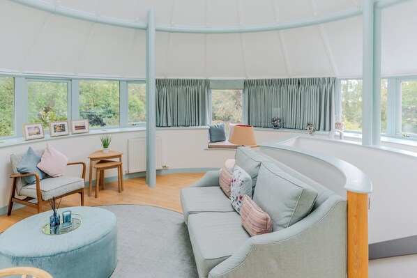 A modern living room with a curved ceiling, a grey sofa, a round ottoman, and a wooden chair. - Retreat to the Water Tower (South Queensferry)