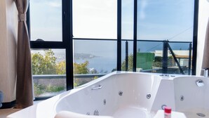 A modern bathroom with a large bathtub, a view of the sea, and a balcony.