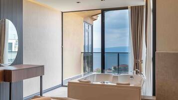 Una habitación de hotel moderna con un ventanal grande, una bañera y un tocador de madera.